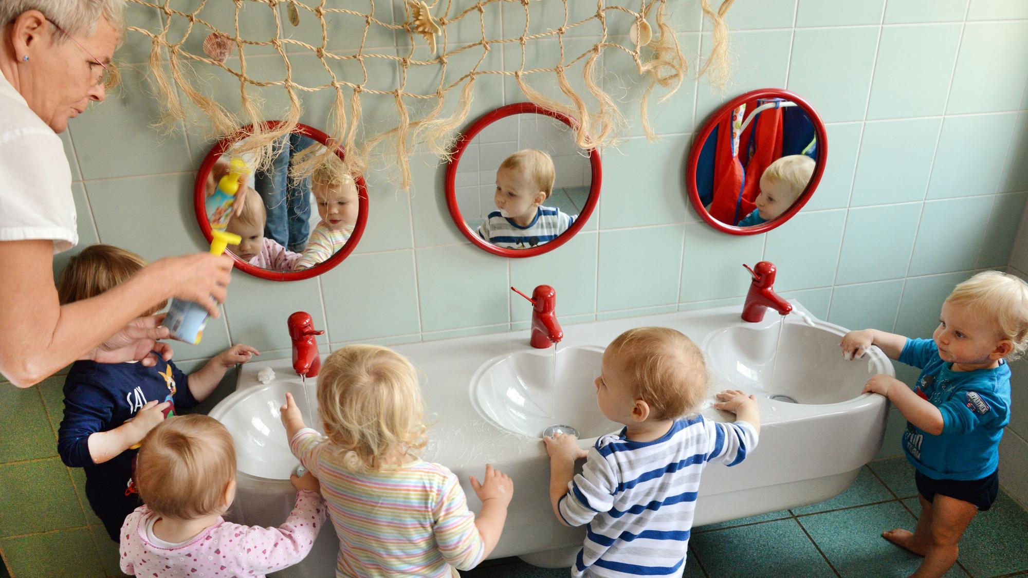 In einer Kita waschen sich die ein-bis zweijährigen Mädchen und Jungen mit ihrer Erzieherin die Hände.
