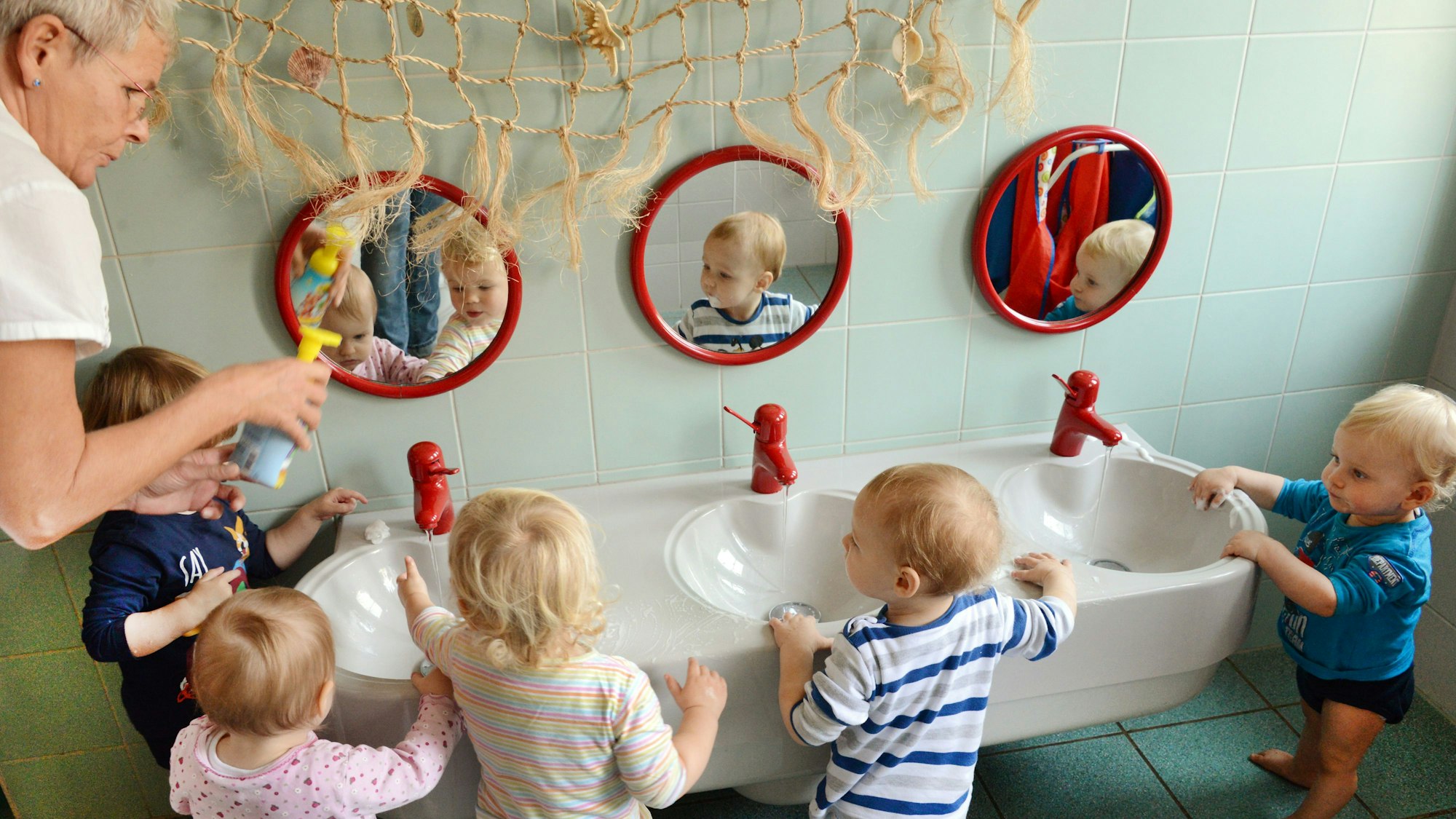 In einer Kita waschen sich die ein-bis zweijährigen Mädchen und Jungen mit ihrer Erzieherin die Hände.