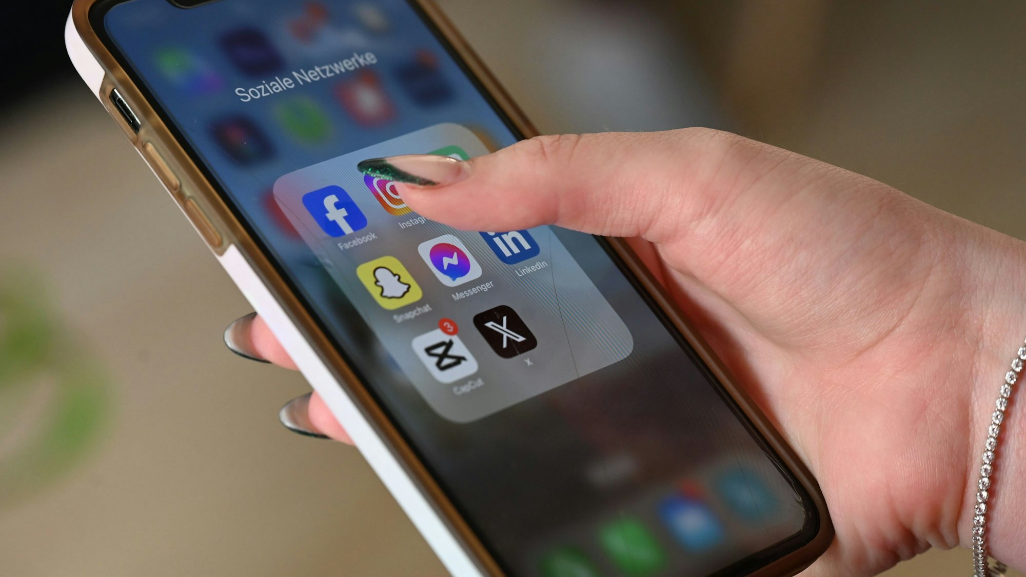 Eine Frau öffnet auf ihrem Smartphone einen Ordner mit Apps verschiedener sozialer Medien.
