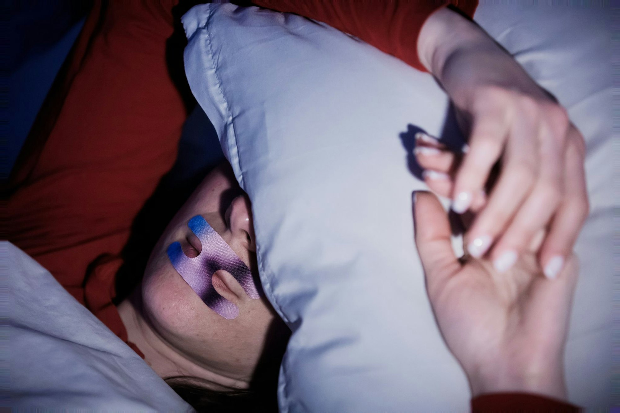 Eine Frau liegt mit einem Mundpflaster im Bett. Ob es hilft? (Illustration)