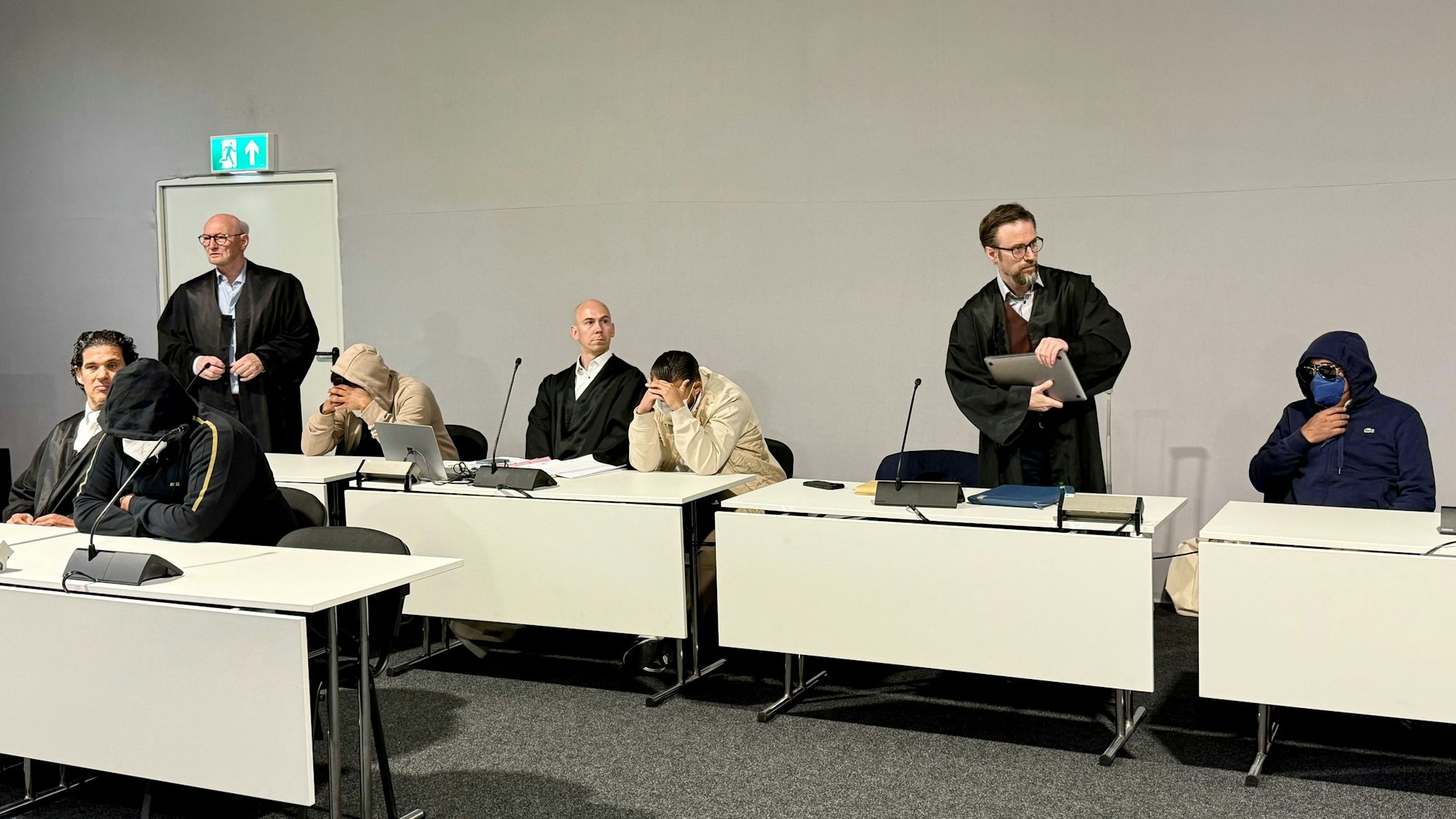 Die vier Angeklagten aus der Leverkusener Großfamilie mit Masken und ihren Verteidigern vor Gericht