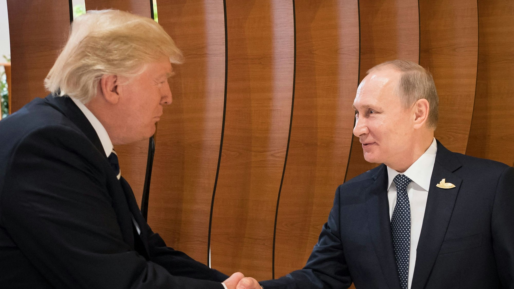 Donald Trump und Wladimir Putin geben sich bei einem Treffen die Hand.