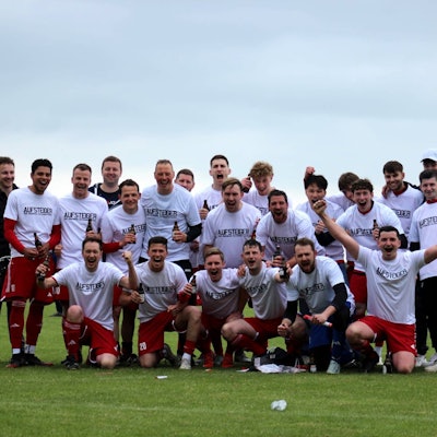 Das Foto zeigt eine Fußball-Mannschaft in weißen Trikots und roten Hosen, die für ein Foto posiert.
