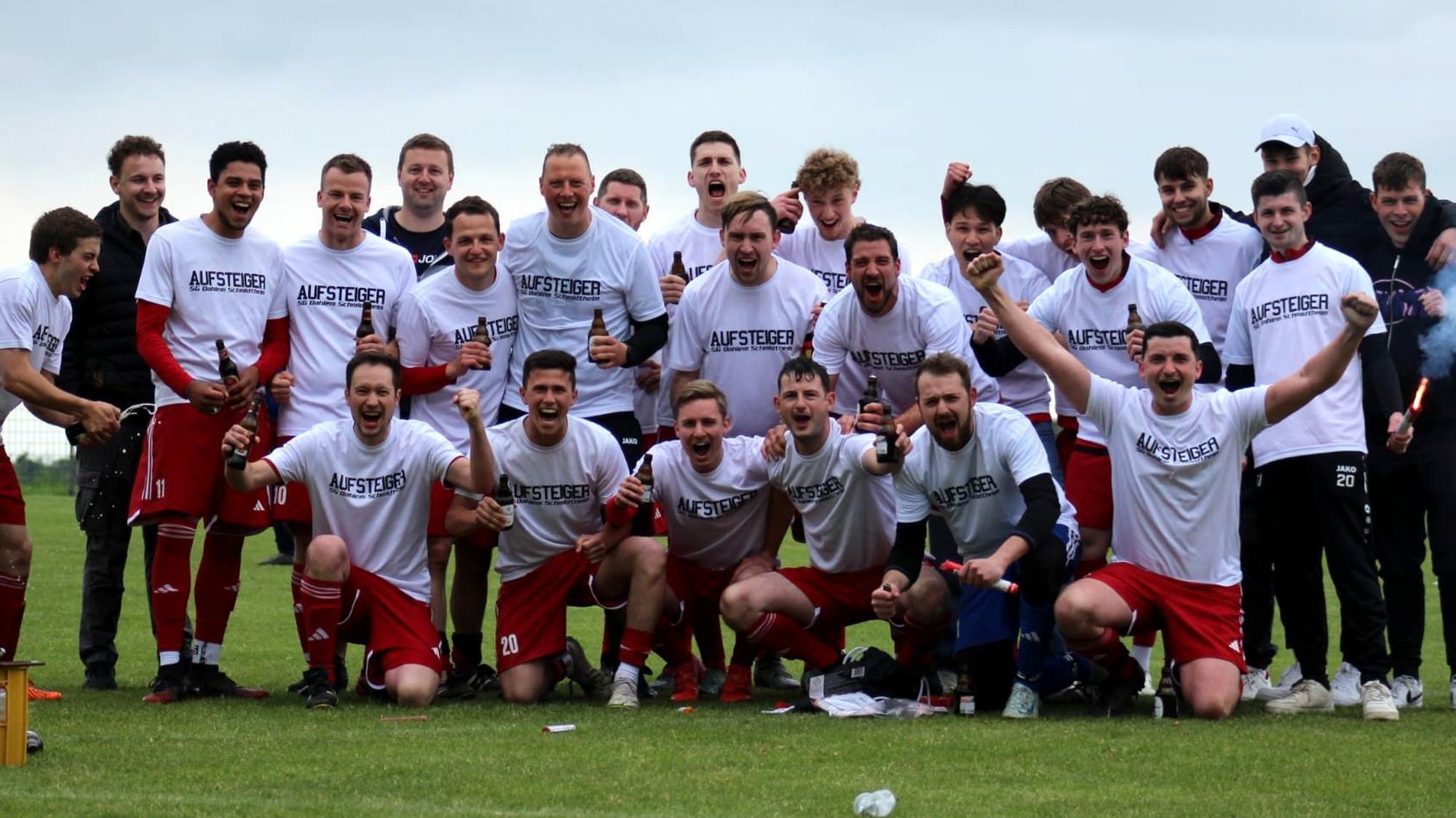 Das Foto zeigt eine Fußball-Mannschaft in weißen Trikots und roten Hosen, die für ein Foto posiert.