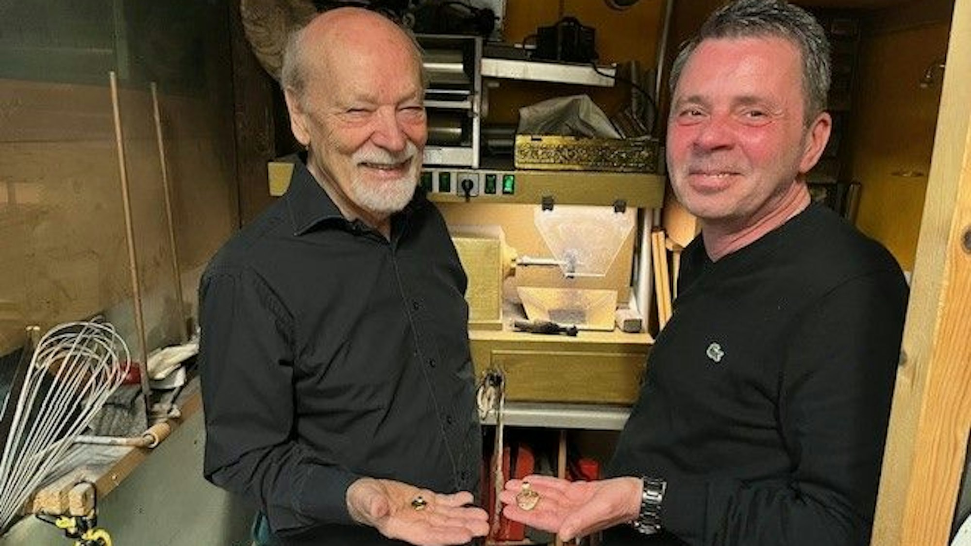 Friseurmeister Ralph Schwalbach und Goldschmiedemeister Herbert Schmelzer sammeln die ersten Schmückstück für die nächste Benefiz-Aktion zugunsten von „wir helfen“. Sie halten goldene Herz-Anhänger in der Hand.