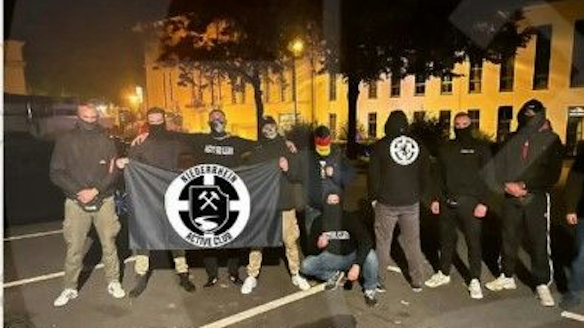 Die Bildsprache der Active Clubs ist eindeutig. Eine Gruppe schwarz vermummter Männer ist zu sehen und eine schwarze Flagge mit weißem Emblem.