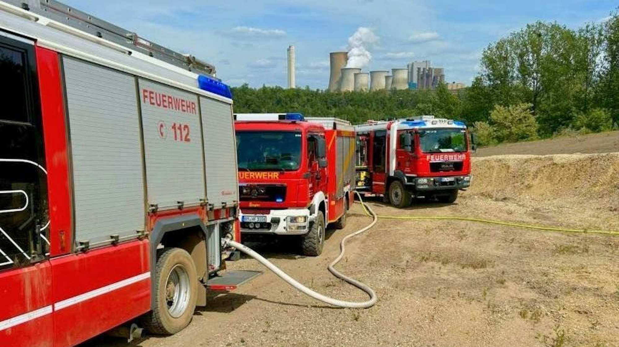 Drei Einsatzwagen stehen auf dem Gelände, im Hintergrund das Kraftwerk Niederaußem.