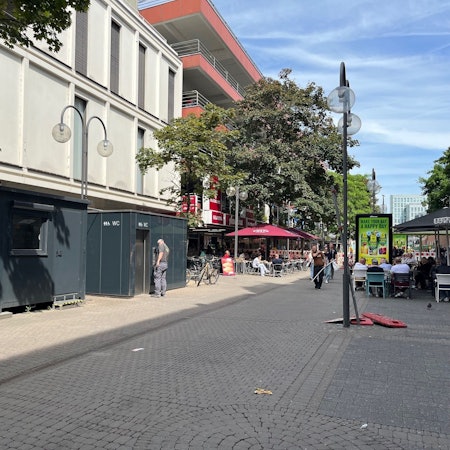 Der Wachmann hat sein Wachhäuschen verlassen und steht vor dem Toilettencontainer.
