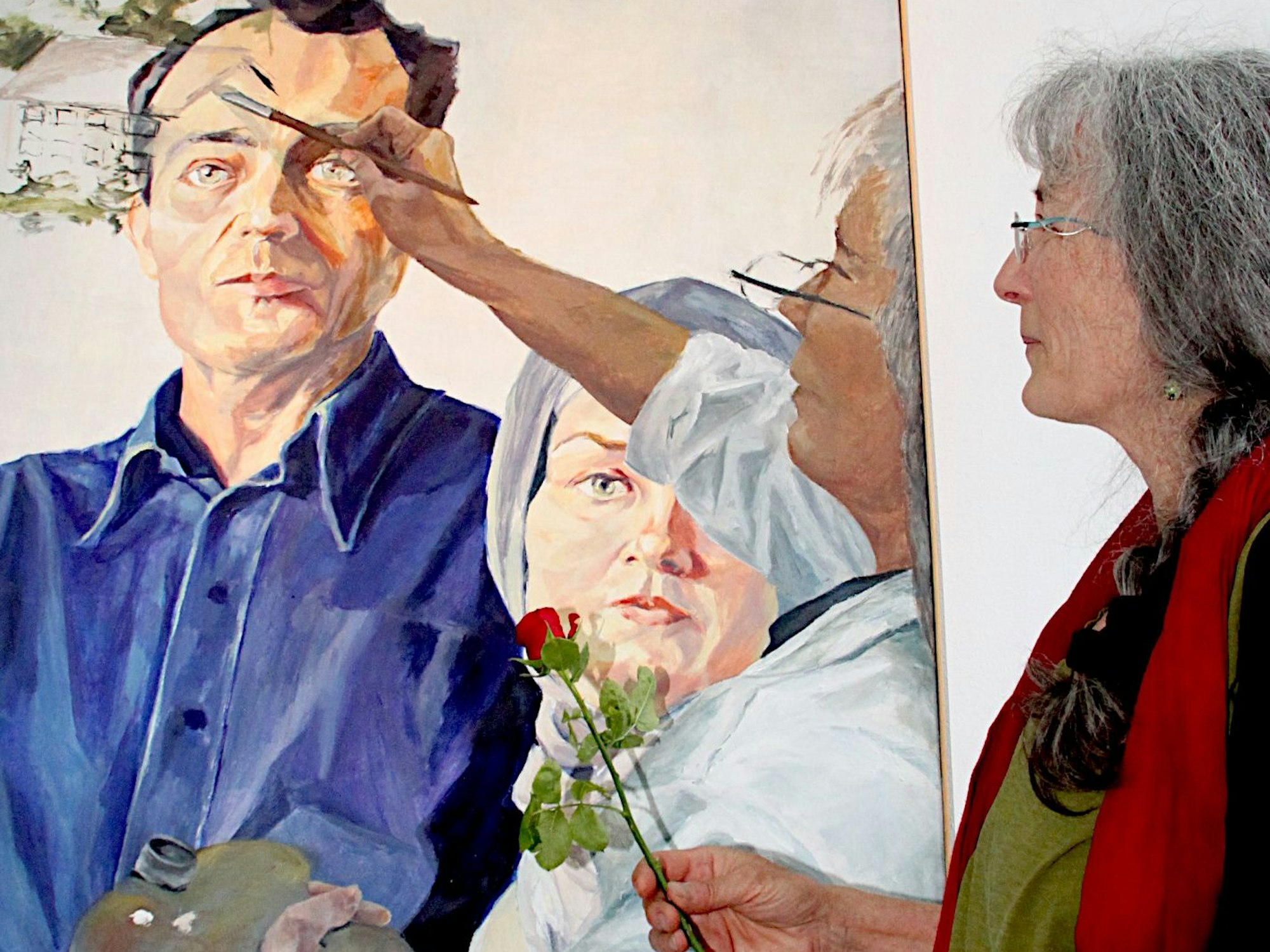 Yvonne Deslile steht neben ihrem Bild „Übermalung des Paares in Scheidung“. Es zeigt ein Paar im unterkühlten Stil der Neuen Sachlichkeit und sich selbst am Bildrand als die, die dieses Idealbild gerade übermalt.