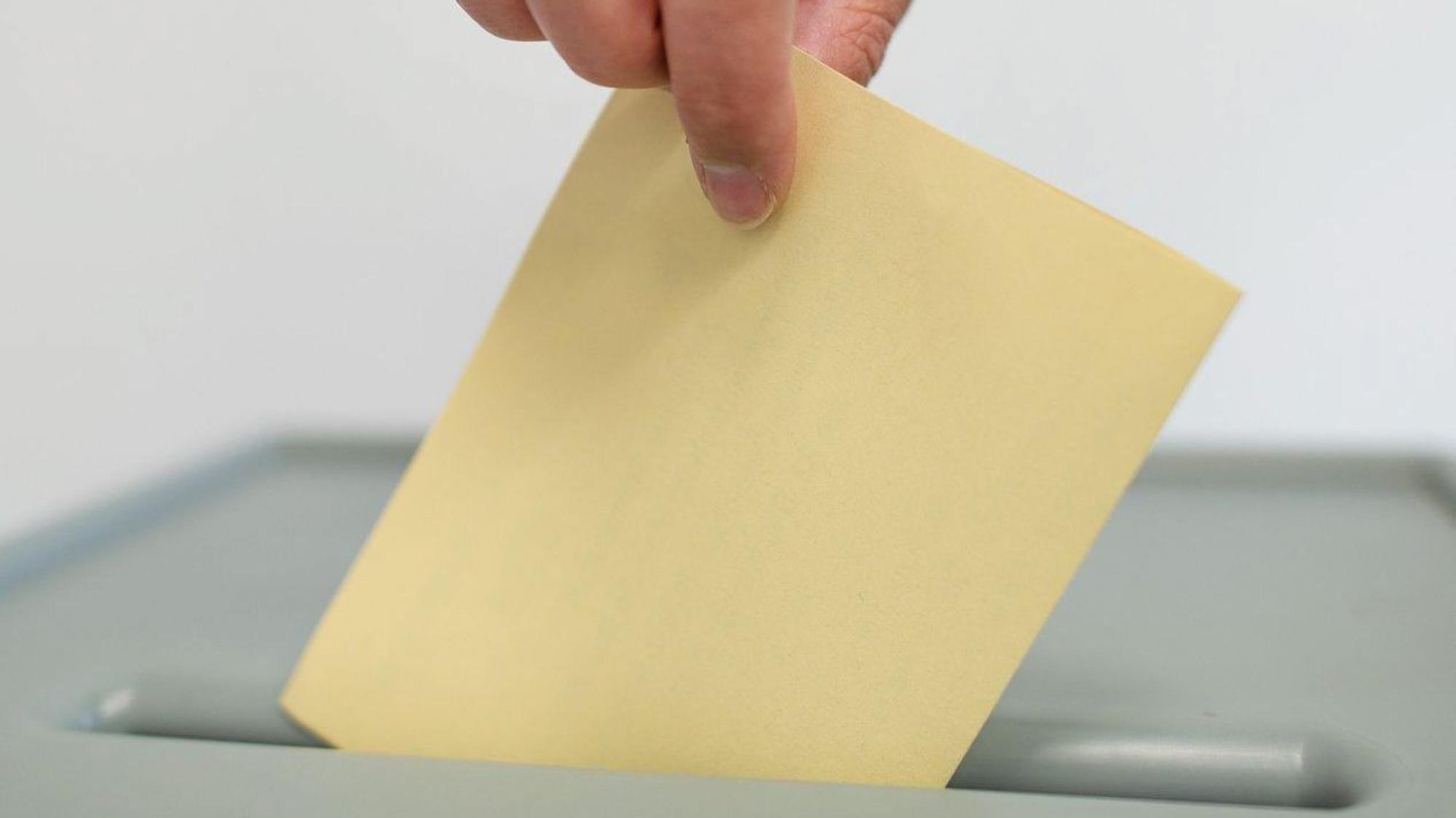 Ein Stimmzettel für den einen Bürgerentscheid wird in eine Wahlurne geworfen.