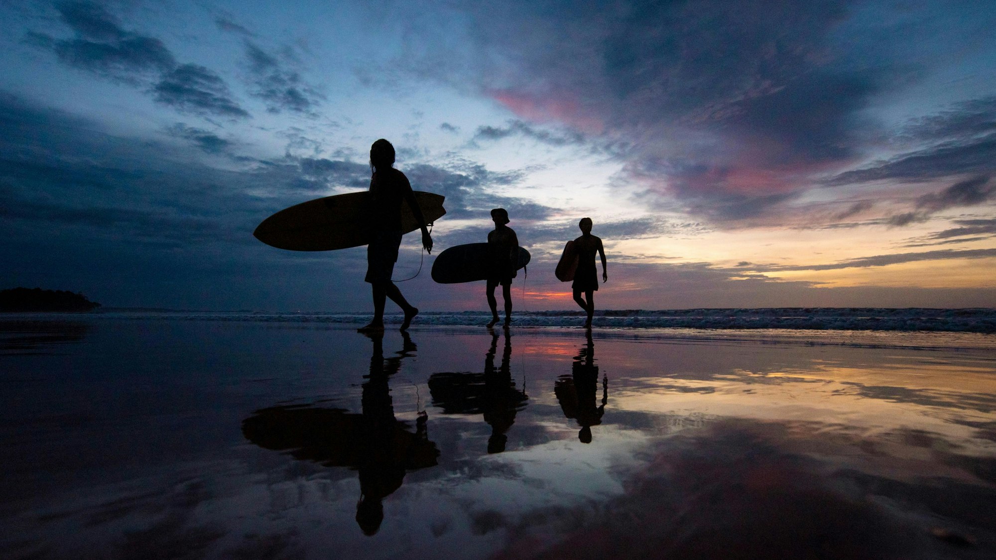 Eine Gruppe einheimischer Surfer geht sie in der Abenddämmerung über den Strand Sungai Pagar in Labuan. Surfen wird auch in Malaysia immer beliebter.