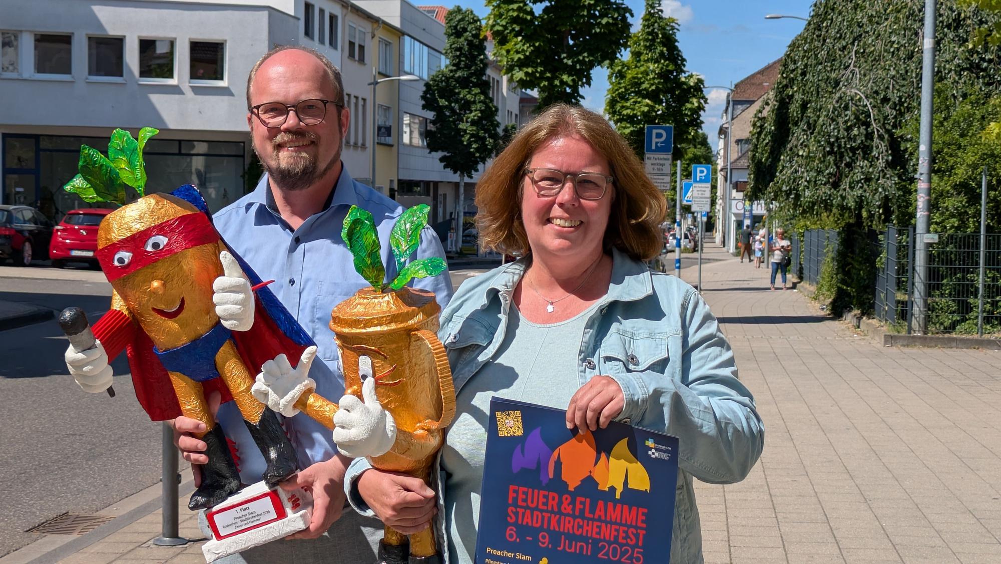Das Bild zeigt Annette Kleinertz und Gregor Weichsel mit Pokalen und Plakaten.
