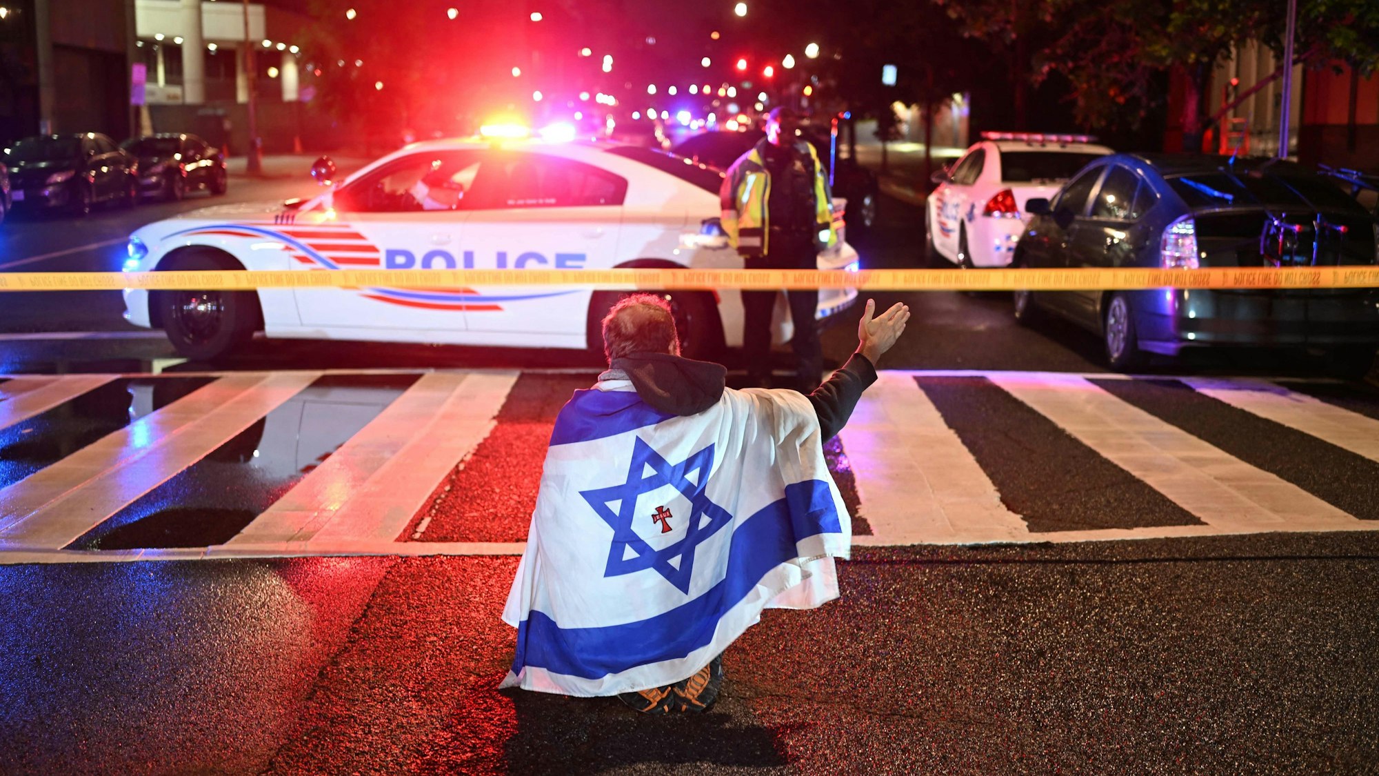 Ein Mann, der die israelische Flagge mit einem Kreuz und dem Namen „Jesus“ in der Mitte trägt, gestikuliert, während Beamte der Metropolitan Police das Gebiet sichern