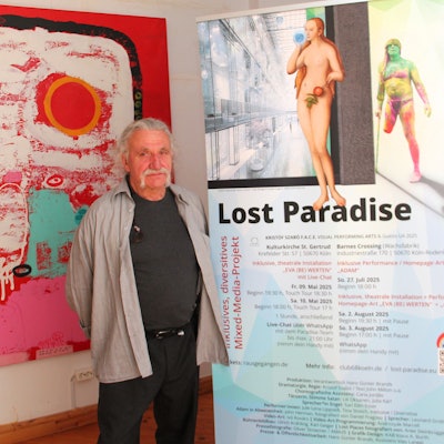 Ein Mann mit grauem Haar und Bart steht zwischen zwei Aufstellern.