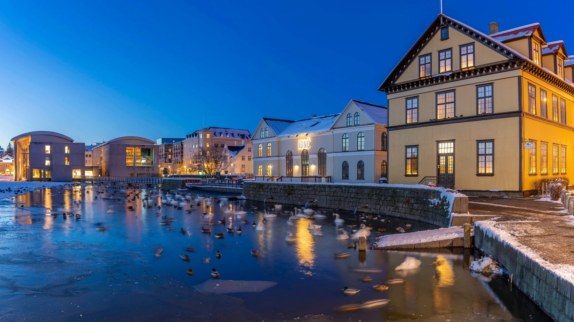 Blick auf Gebäude am Wasser und das Rathaus im Hintergrund im Stadtzentrum von Reykjavik in der Abenddämmerung im Winter, Reykjavik, Island.