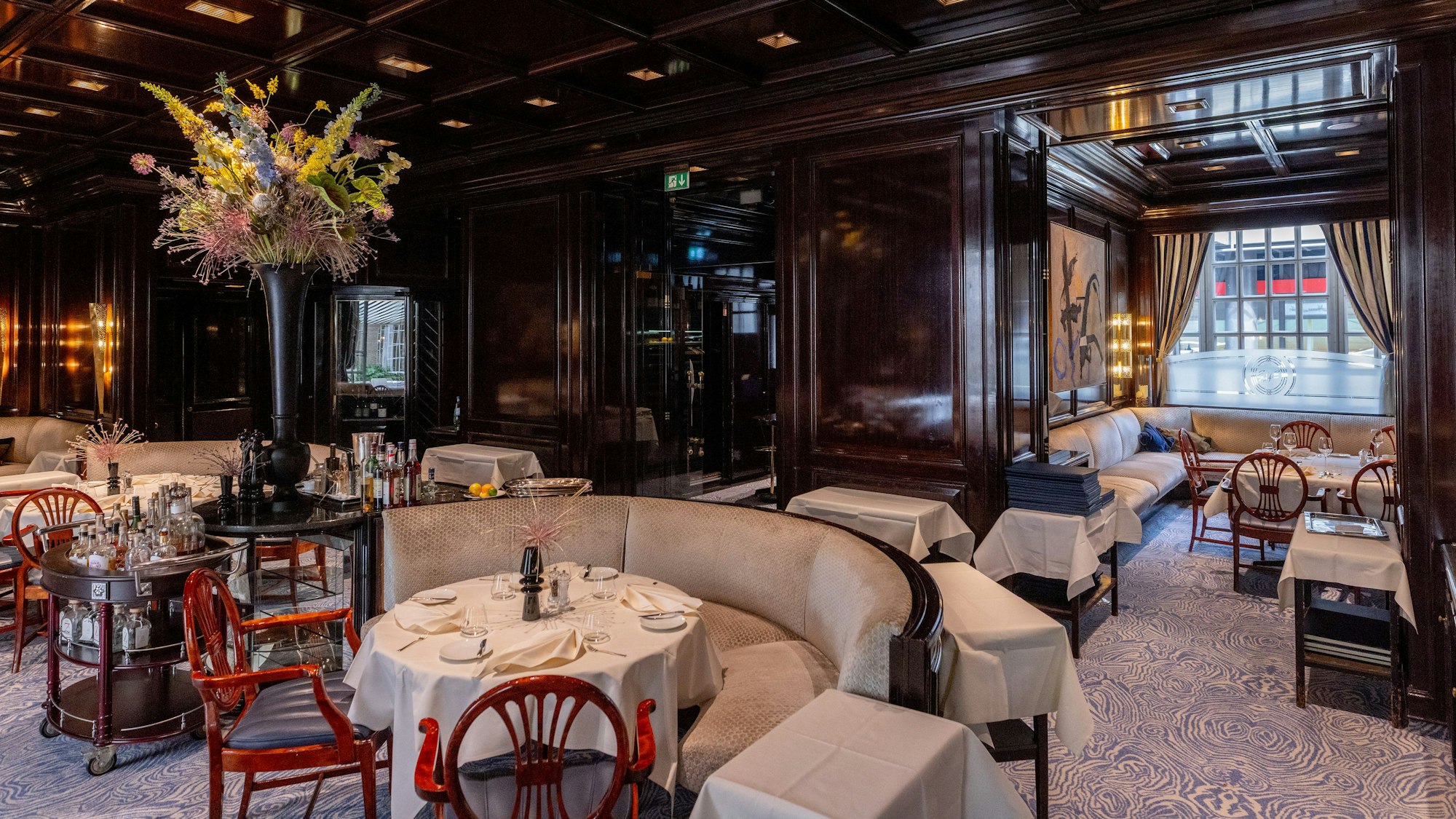 Der Restaurantraum ist zu sehen ohne Gäste. Hell bespanntes Holzmobiliar, dunkel getäfelte Wände und Decke.