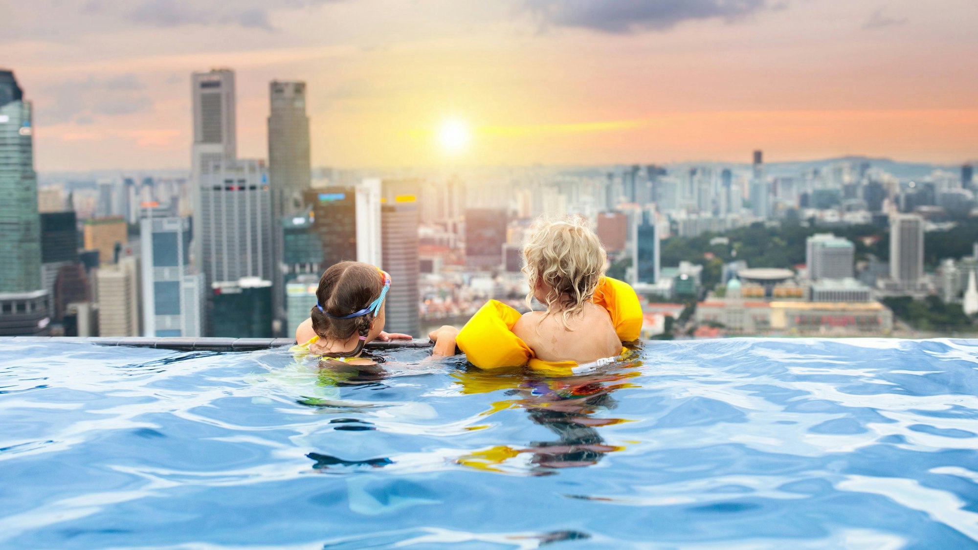 Kinder schwimmen im Außenpool auf dem Dach im Familienurlaub in Singapur.