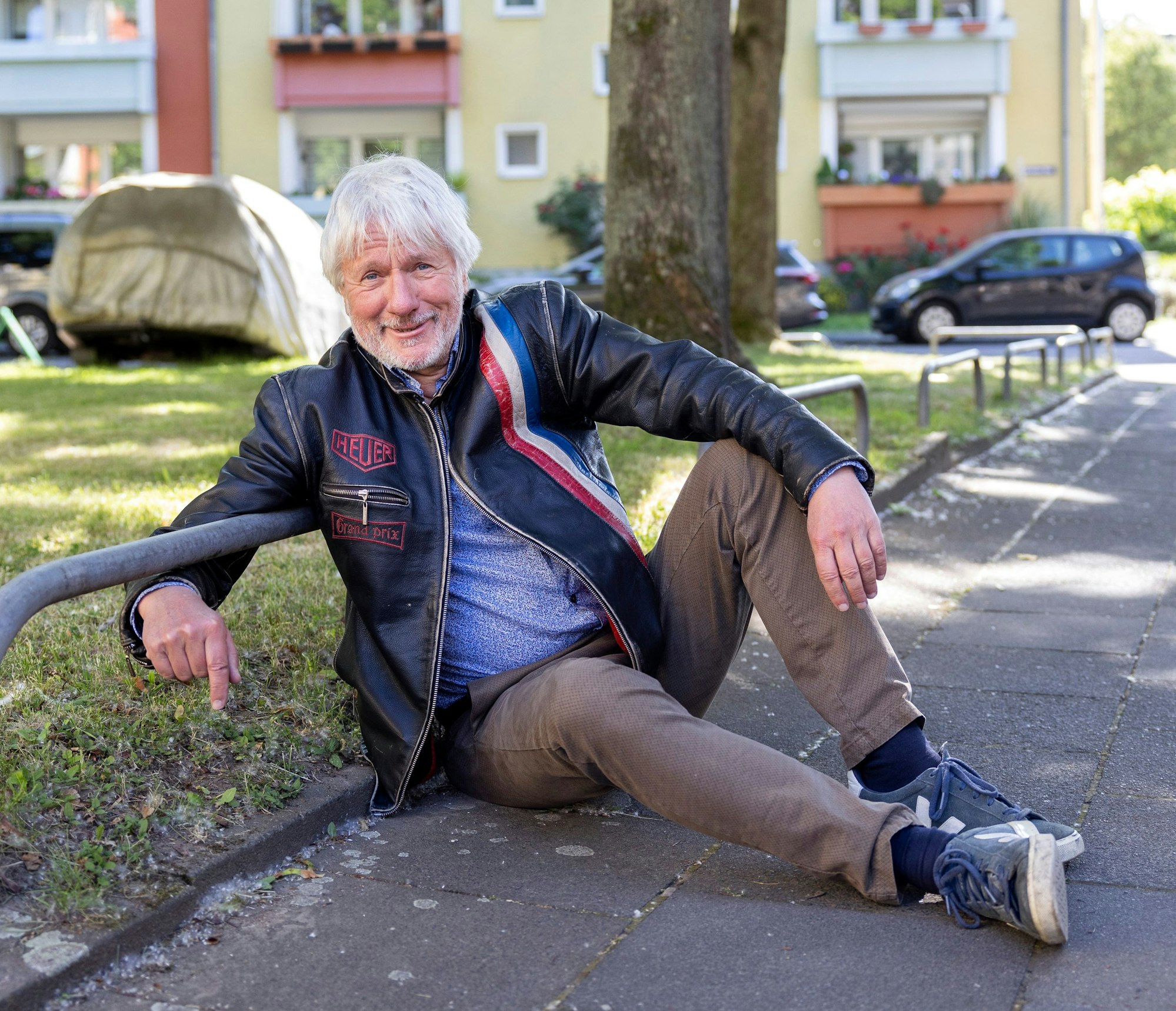 Ein Mann sitzt auf dem Bürgersteig am Rande einer von Metall-Absperrungen begrenzten Grünfläche.
