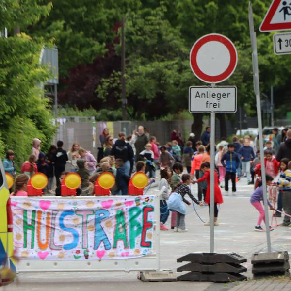 Zu sehen ist ein Banner mit der Aufschrift „Schulstraße“ und dahinter spielende Kinder.
