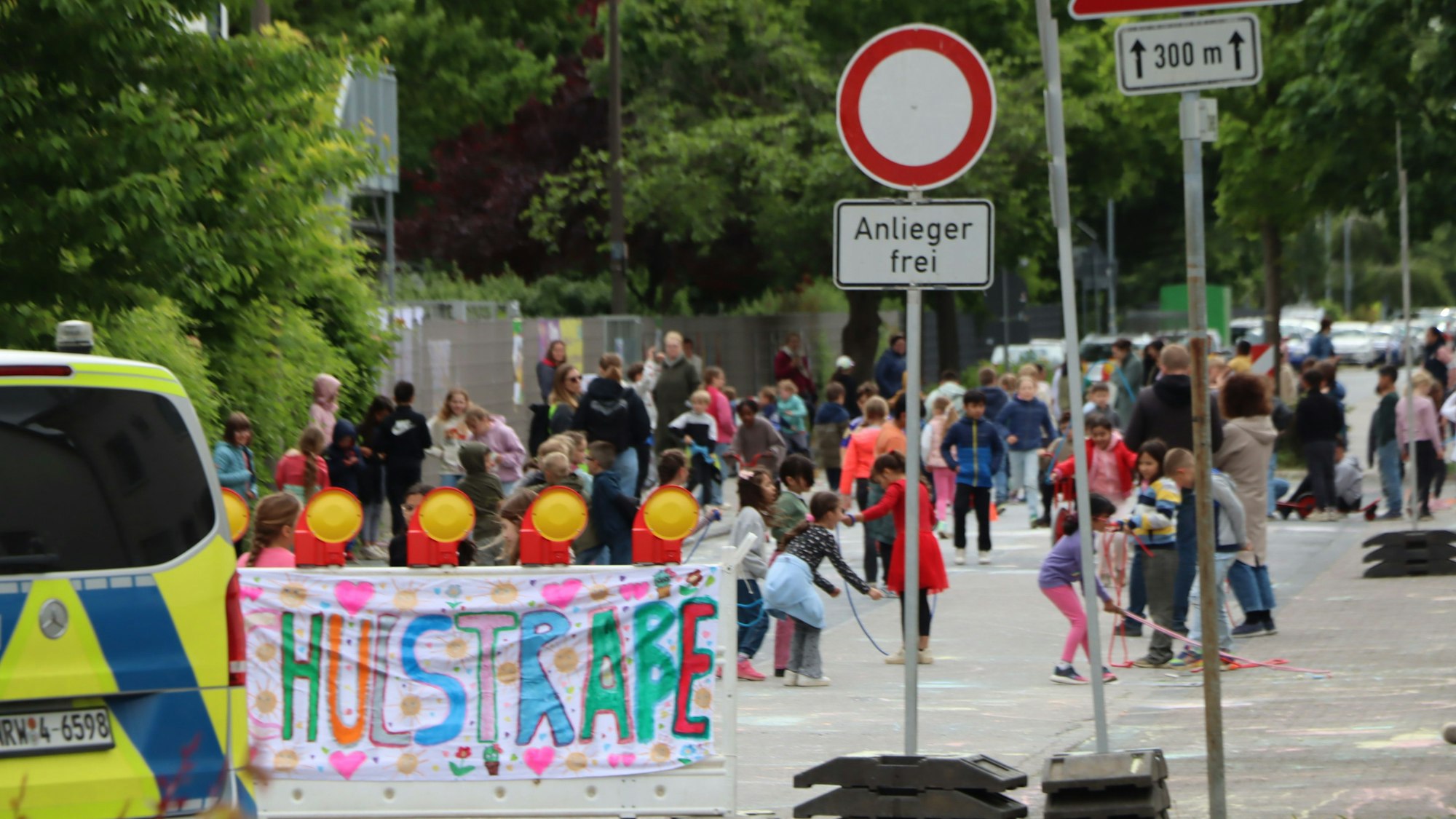 Zu sehen ist ein Banner mit der Aufschrift „Schulstraße“ und dahinter spielende Kinder.