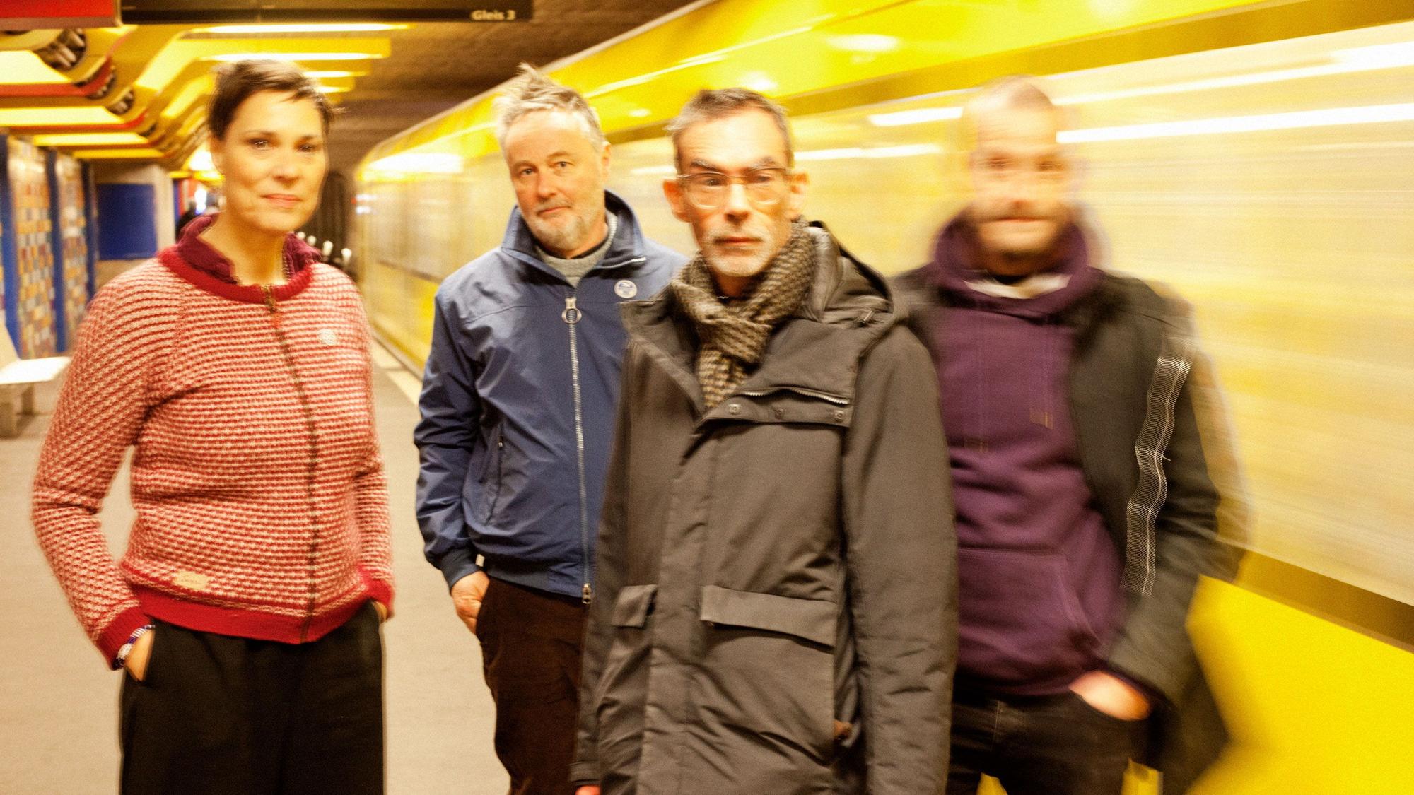 Die Band Stereolab posiert vor einer fahrenden U-Bahn.