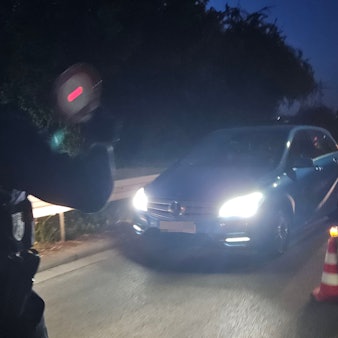Ein Polizist winkt mit einer roten Kelle ein Fahrzeug aus dem Verkehr.