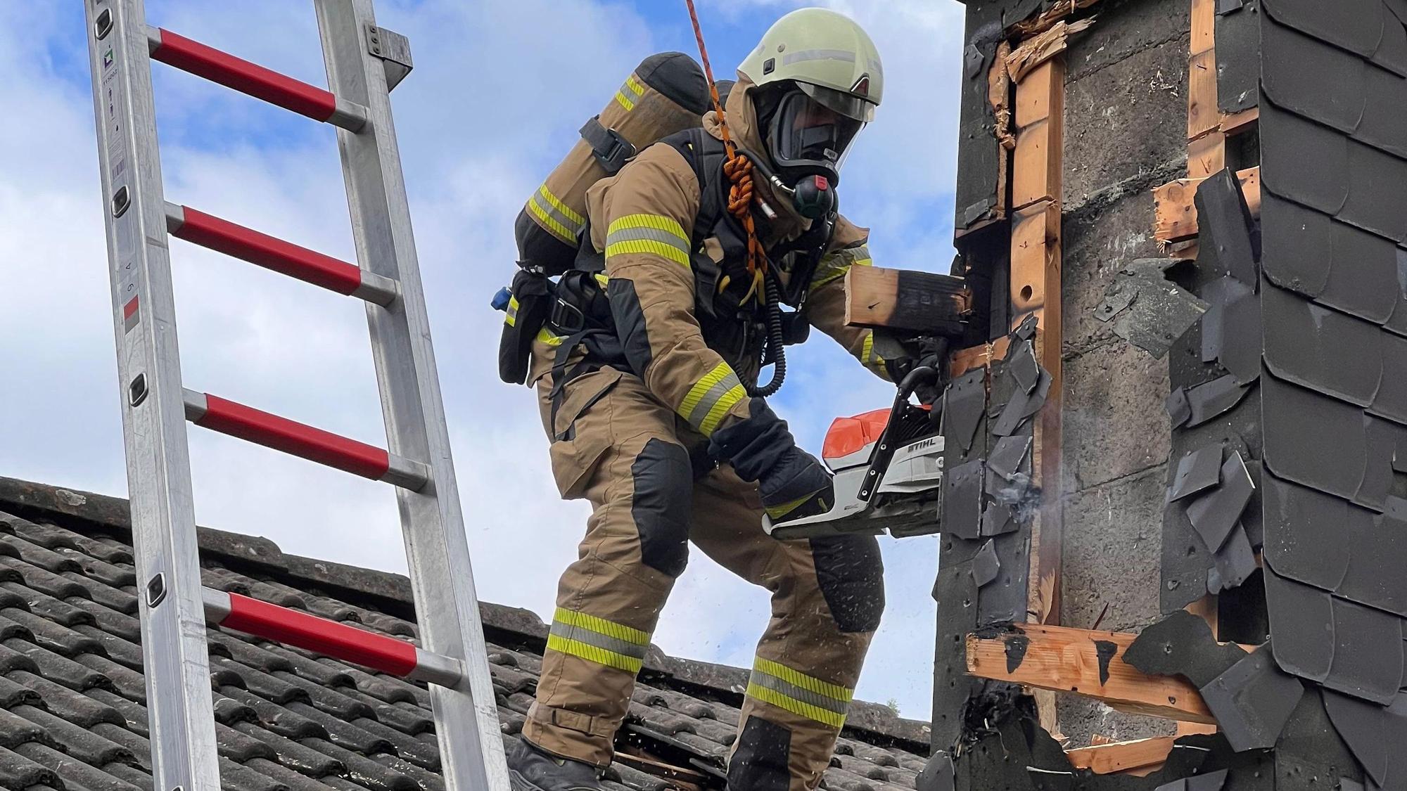 Ein Feuerwehrmann öffnet einen Kamin mit einer Motorsäge.