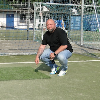 Ein Mann zeigt auf neuen und alten Kunstrasen auf einem Kunstrasen-Fußballplatz.