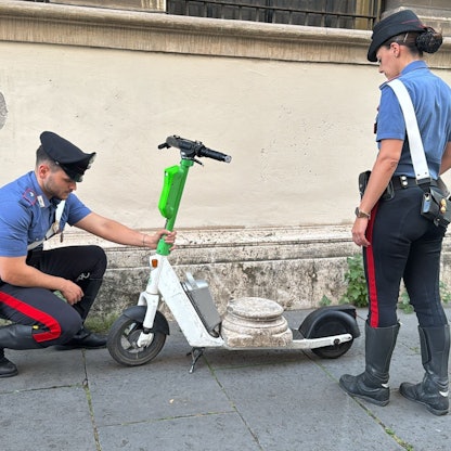 Zwei Carabiniere stehen neben dem E-Scooter mit der antiken Marmorsockelplatte.