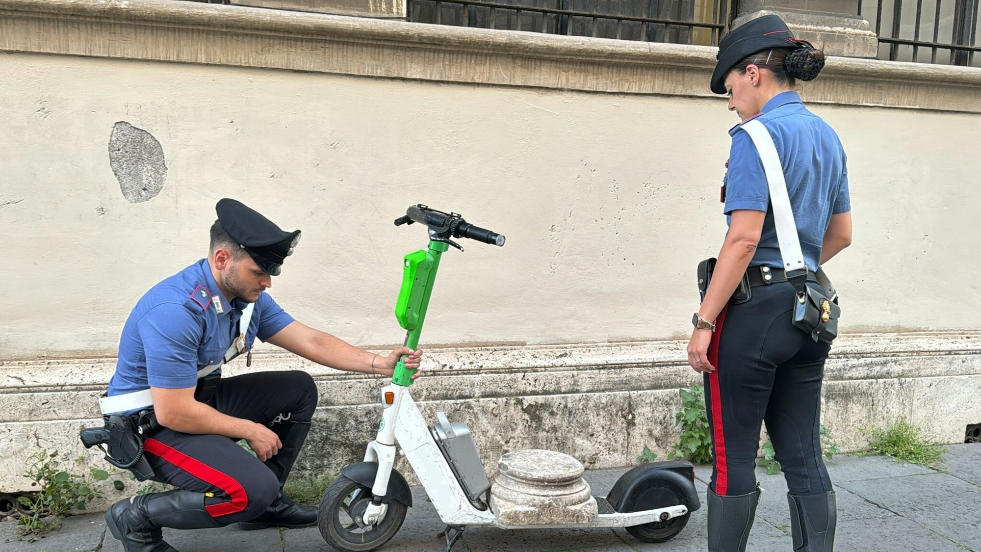 Zwei Carabiniere stehen neben dem E-Scooter mit der antiken Marmorsockelplatte.