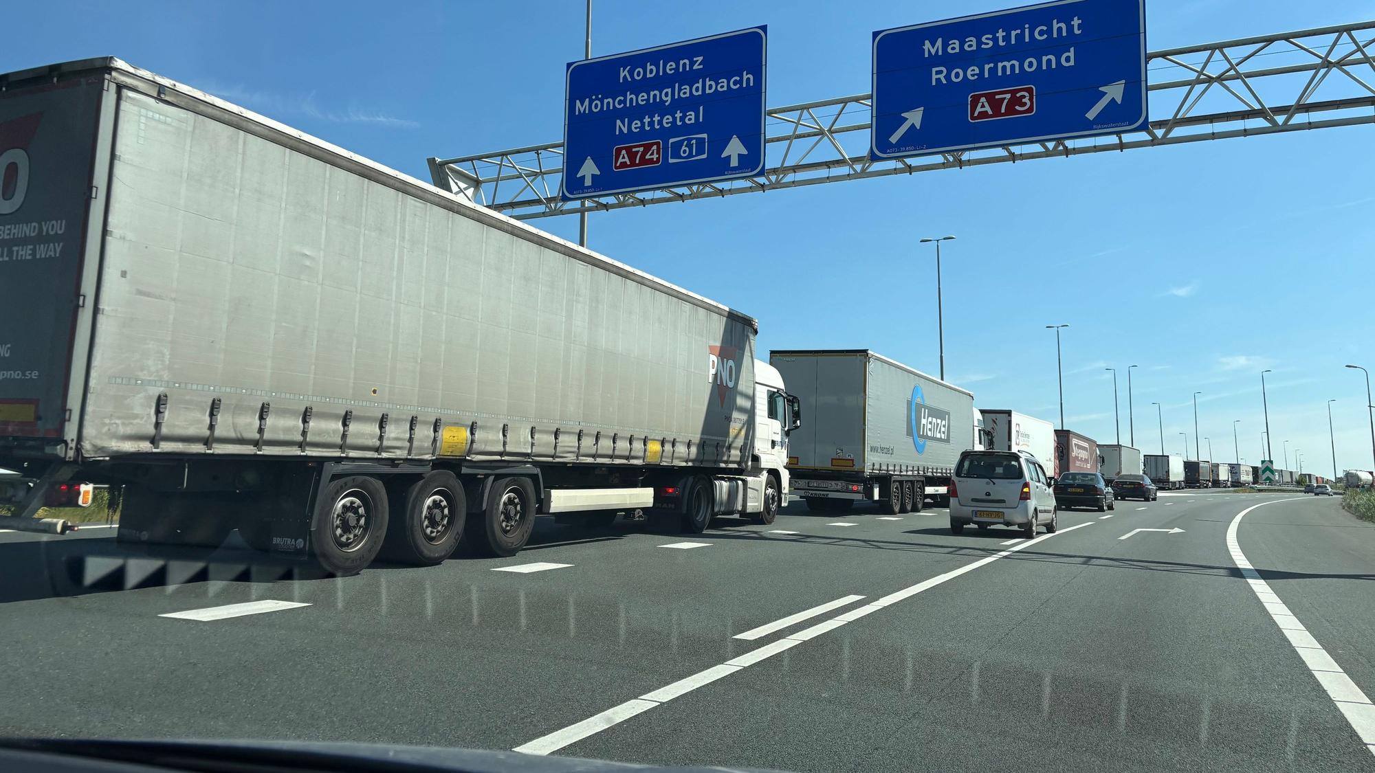 LKW stehen hintereinander im Stau. Über ihnen hängt ein Schild mit der Aufschrift „Koblenz“, darunter „Mönchengladbach“ und „Nettetal“, „A 74 61“.