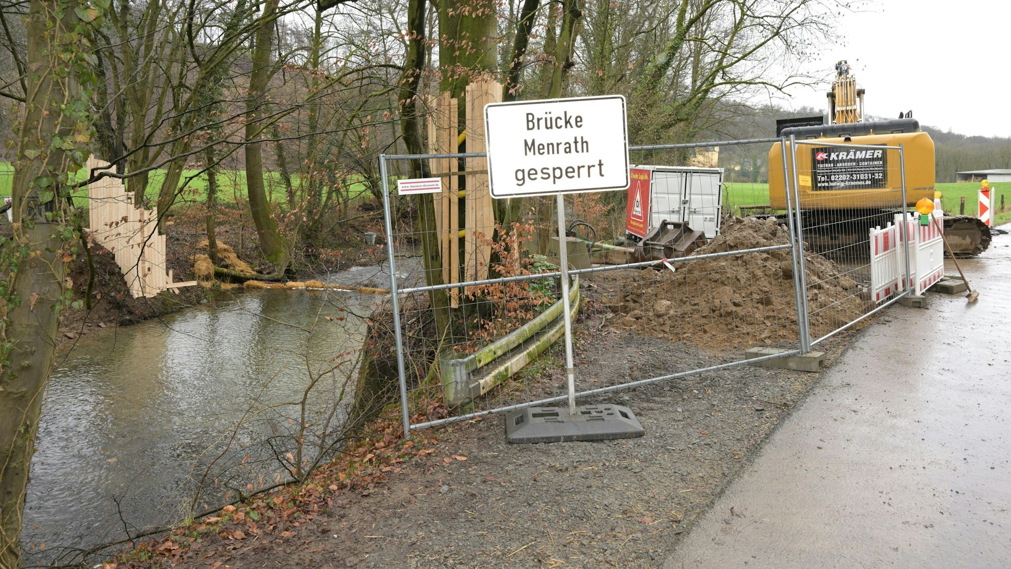 Ein Fluss, davor ein Bauzaun und ein Bagger, im Wasser die Reste einer Brücke.