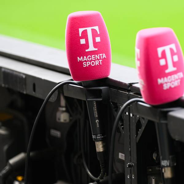 Mikrofone von Magenta Sport stecken an einer Bande in einem Fußballstadion. (Archivbild)