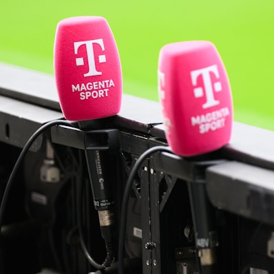 Mikrofone von Magenta Sport stecken an einer Bande in einem Fußballstadion. (Archivbild)
