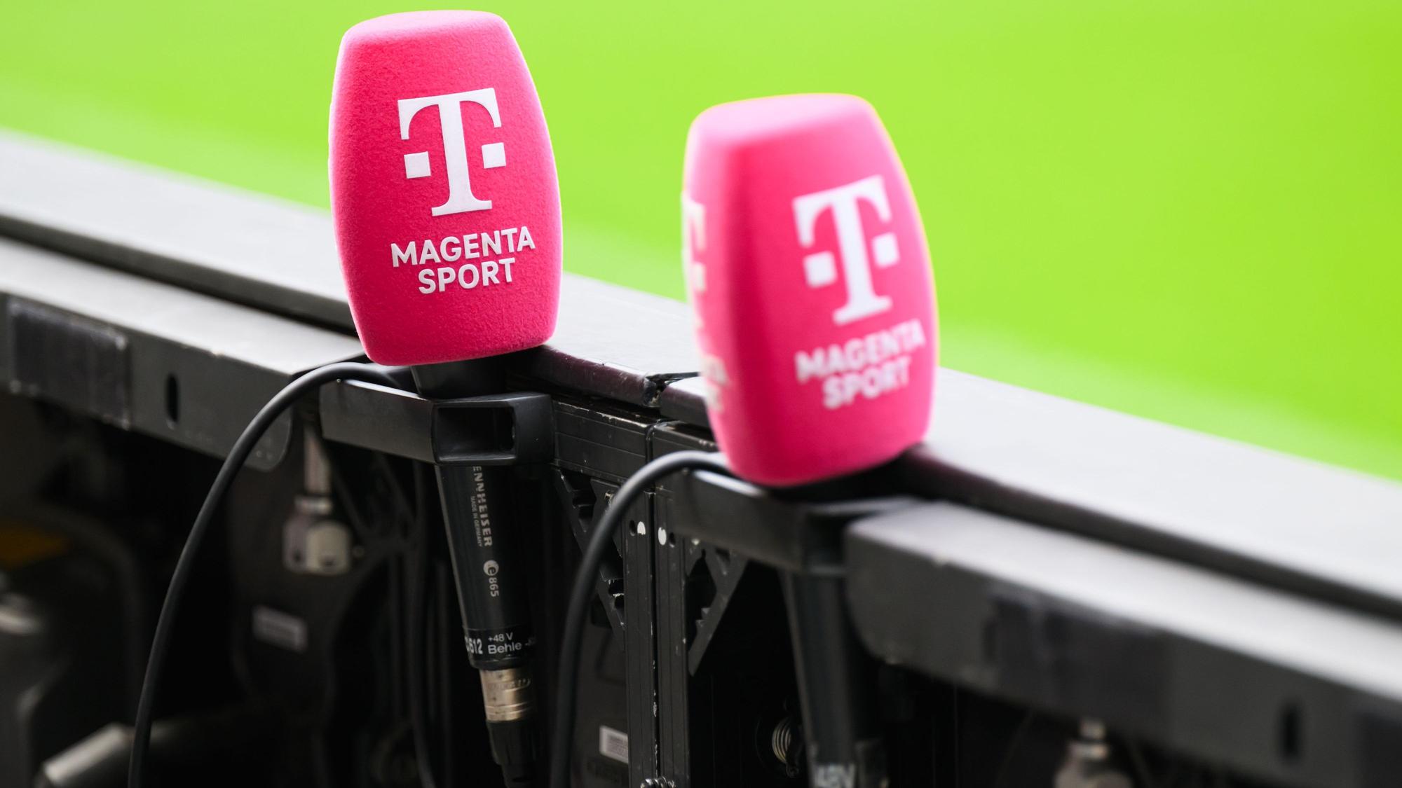 Mikrofone von Magenta Sport stecken an einer Bande in einem Fußballstadion. (Archivbild)
