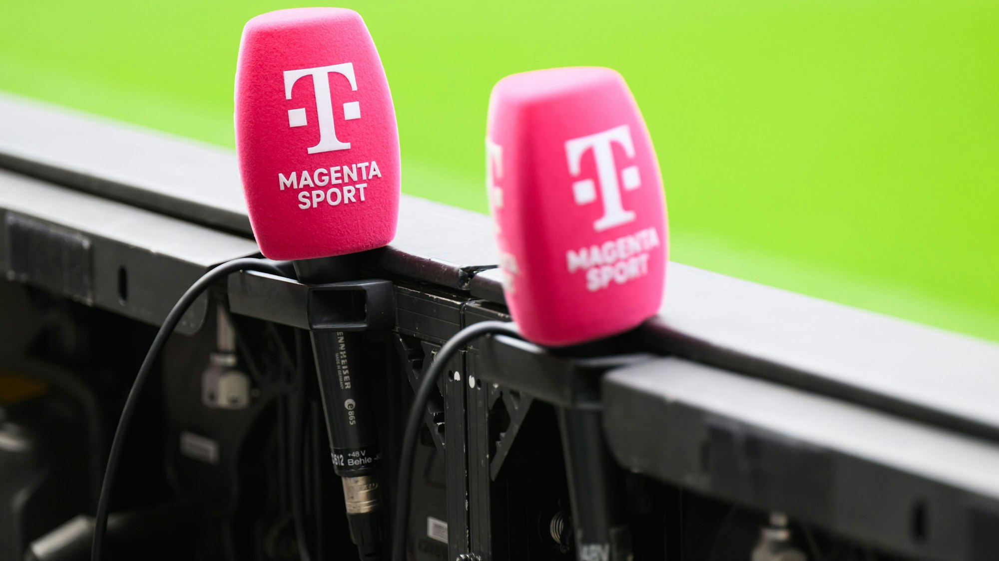 Mikrofone von Magenta Sport stecken an einer Bande in einem Fußballstadion. (Archivbild)