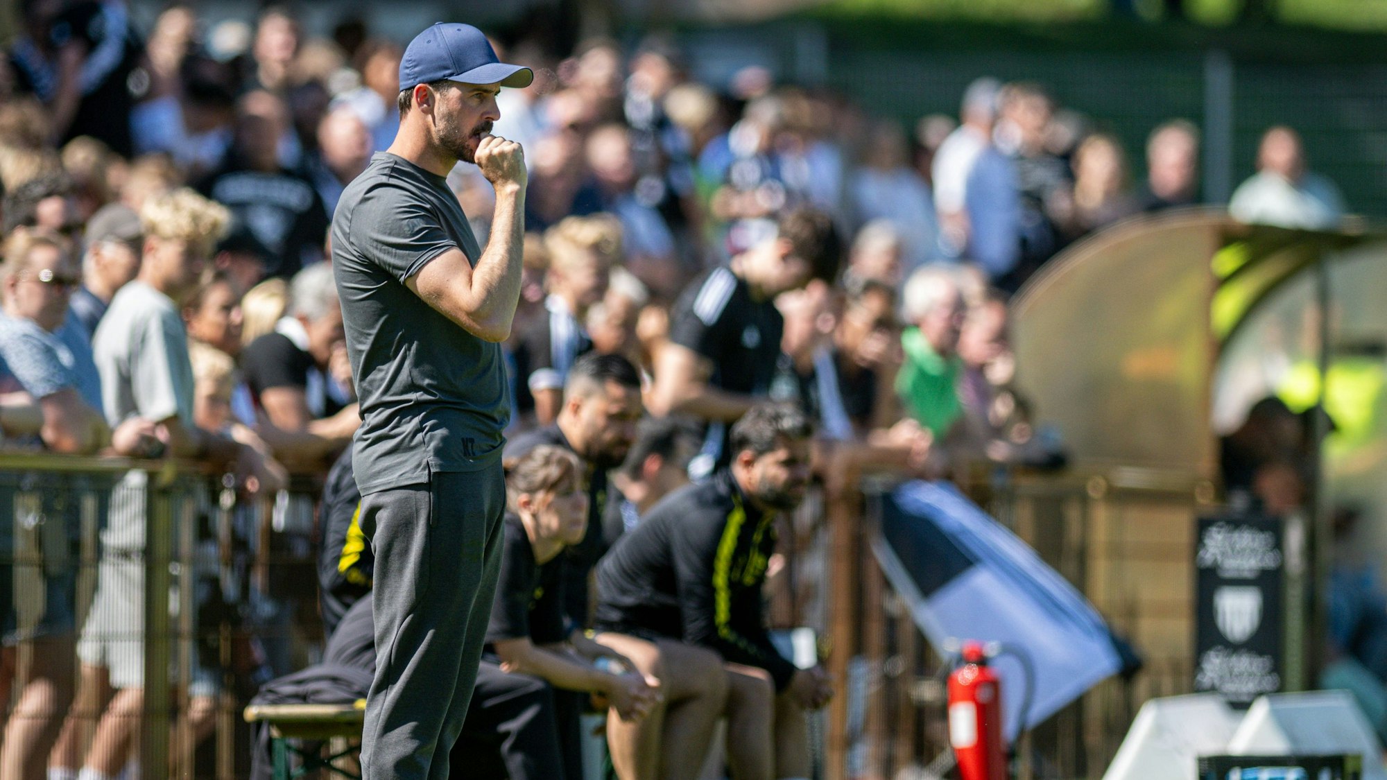 Zu sehen ist ein Fußballtrainer, der an der Seitenlinie steht.