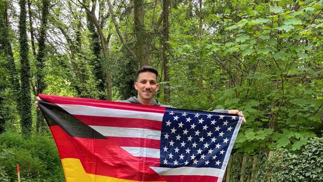 Sufjan Ato Shawrdi mit einer Flagge, die geteilt die deutschen und die US-amerikanischen Farben zeigt.