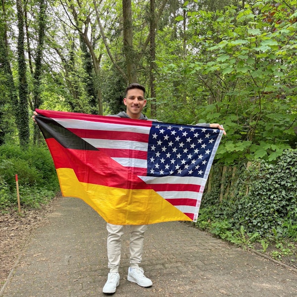 Sufjan Ato Shawrdi mit einer Flagge, die geteilt die deutschen und die US-amerikanischen Farben zeigt.