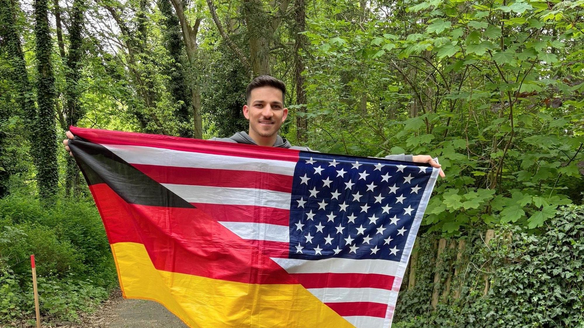 Sufjan Ato Shawrdi mit einer Flagge, die geteilt die deutschen und die US-amerikanischen Farben zeigt.