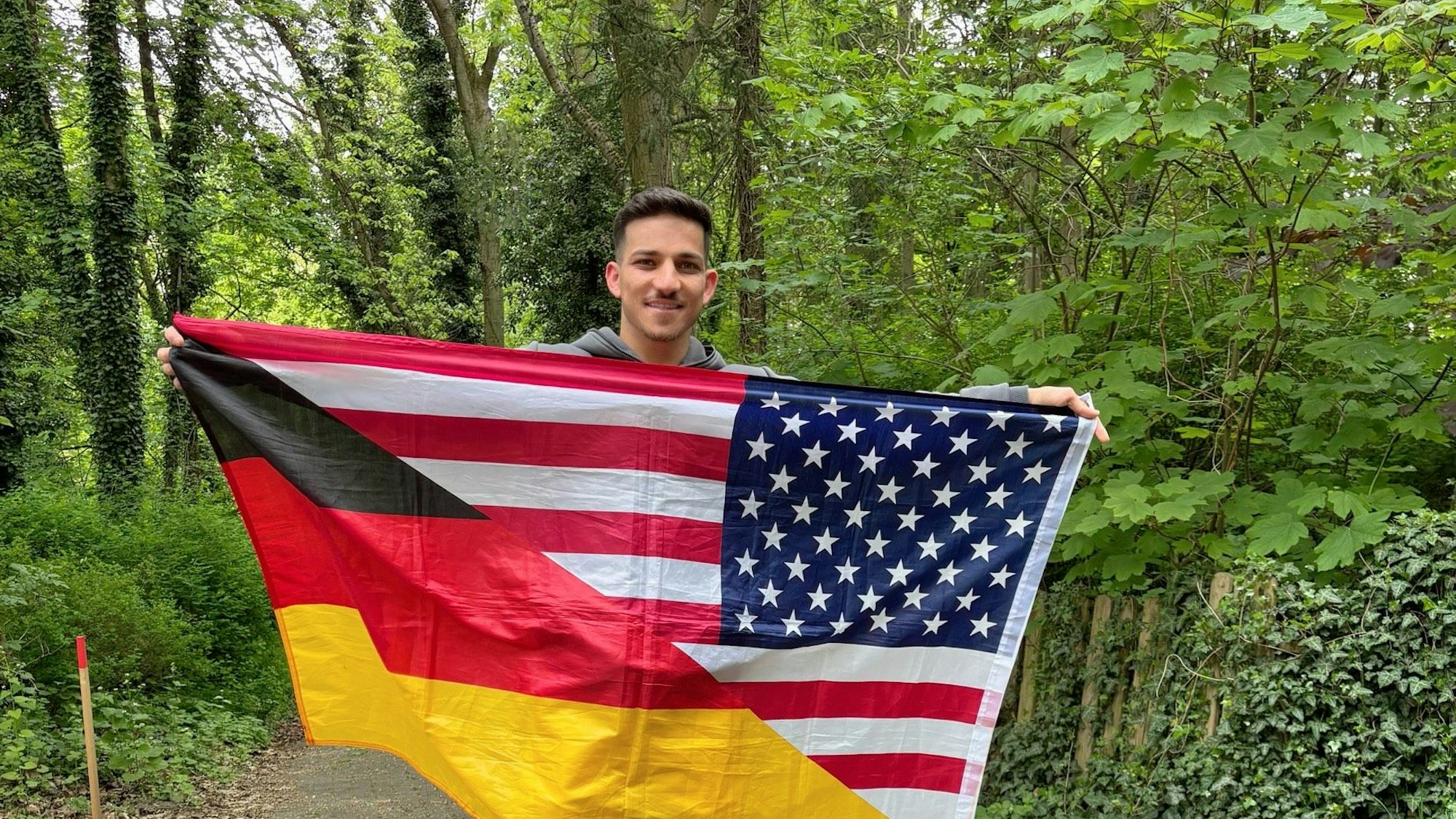 Sufjan Ato Shawrdi mit einer Flagge, die geteilt die deutschen und die US-amerikanischen Farben zeigt.