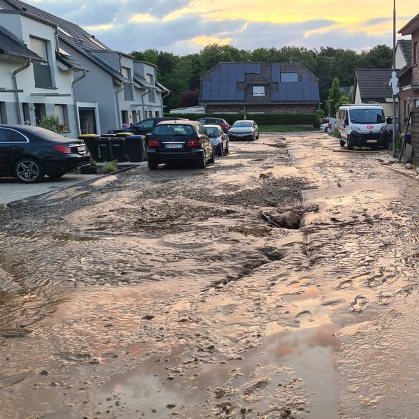 Das Foto zeigt eine verschlammte Straße, an der Seite steht ein Einsatzfahrzeug der Feuerwehr.
