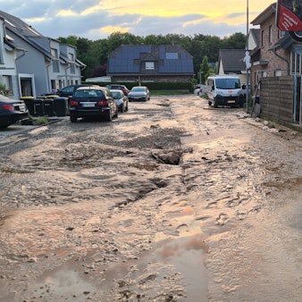 Das Foto zeigt eine verschlammte Straße, an der Seite steht ein Einsatzfahrzeug der Feuerwehr.