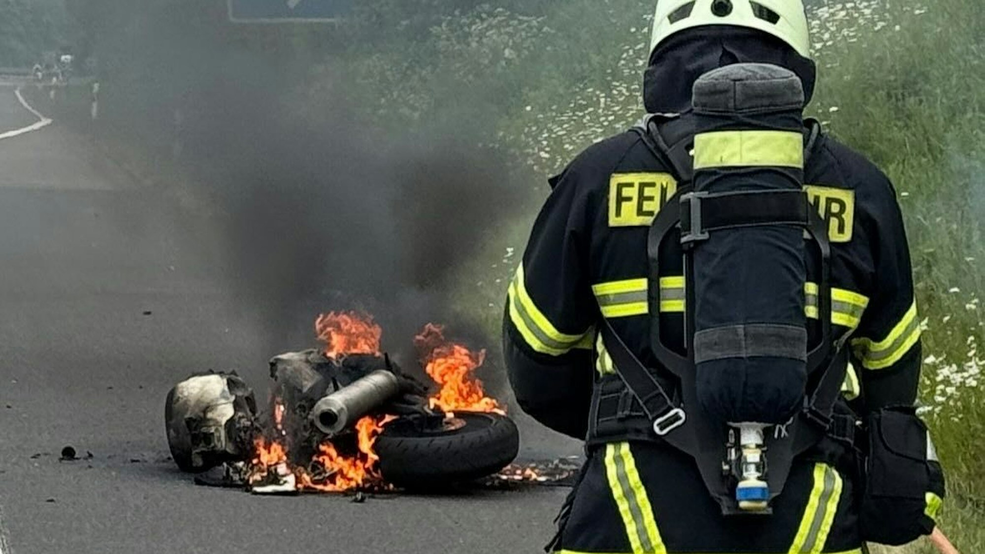 Ein Feuerwehrmann steht in mehreren Metern Entfernung vor einem brennenden Motorrad.