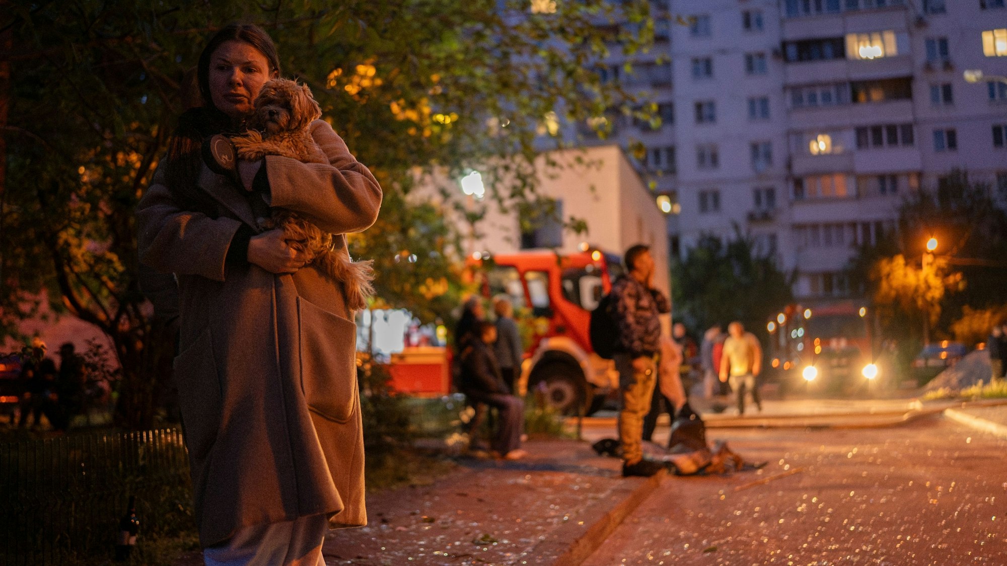 24.05.2025, Ukraine, Kiew: Eine Frau trägt ihren Hund, während sie auf einer Straße mit Glasscherben an der Stelle eines Wohnhauses geht, das durch einen russischen Angriff beschädigt wurde. Foto: Alex Babenko/AP/dpa +++ dpa-Bildfunk +++