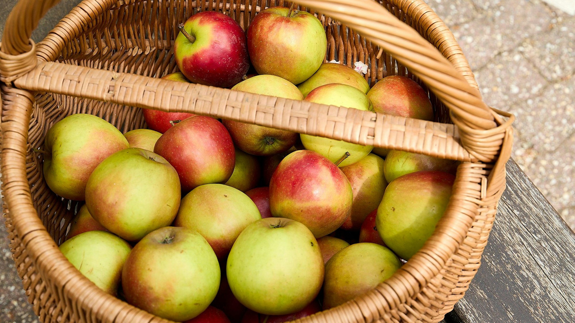 Ein Weidenkorb voll mit Äpfeln steht am Boden.