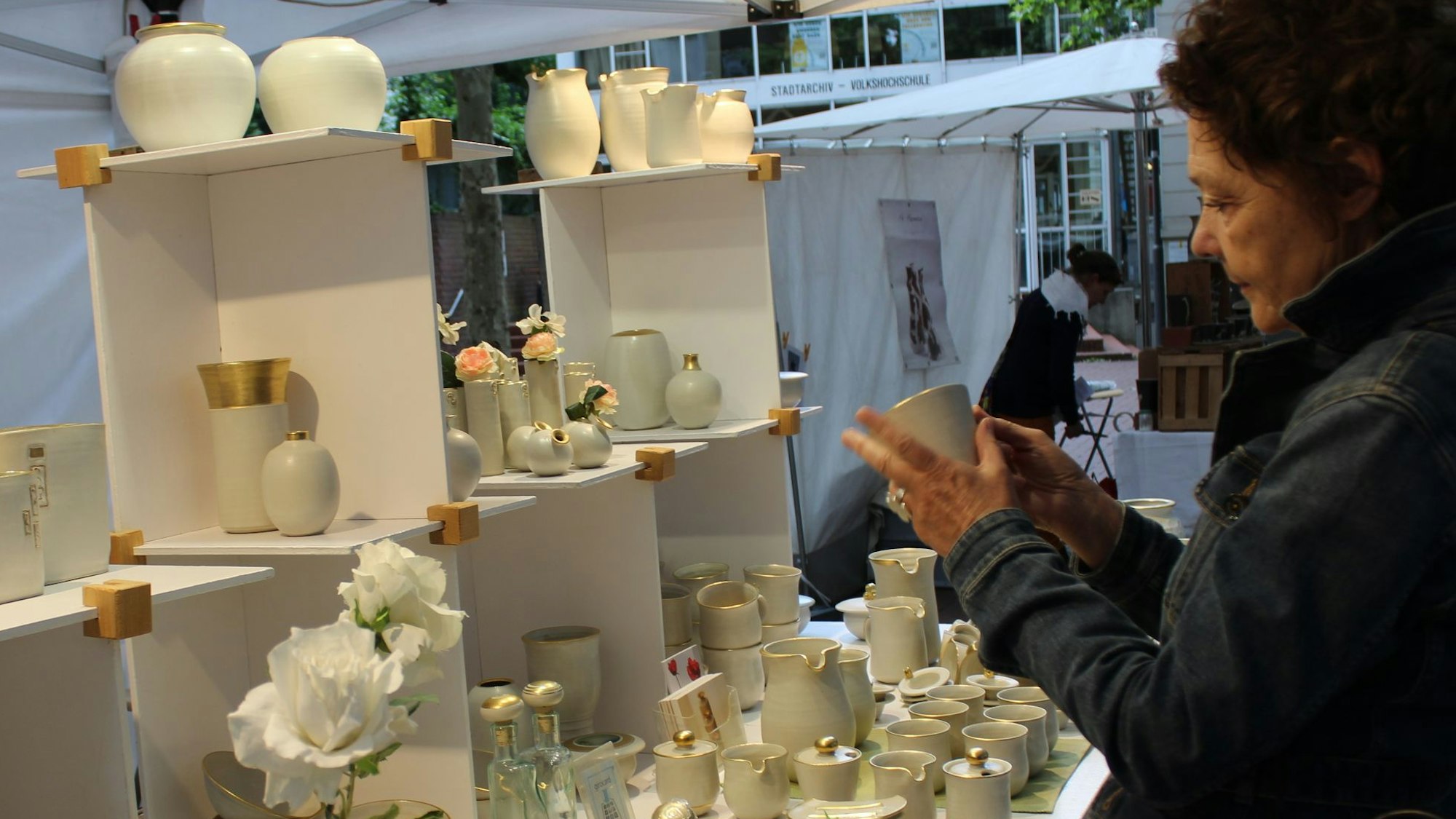 Zu sehen ist eine Besucherin des Töpfermarkts, die eine Tasse in der Hand hält und betrachtet.