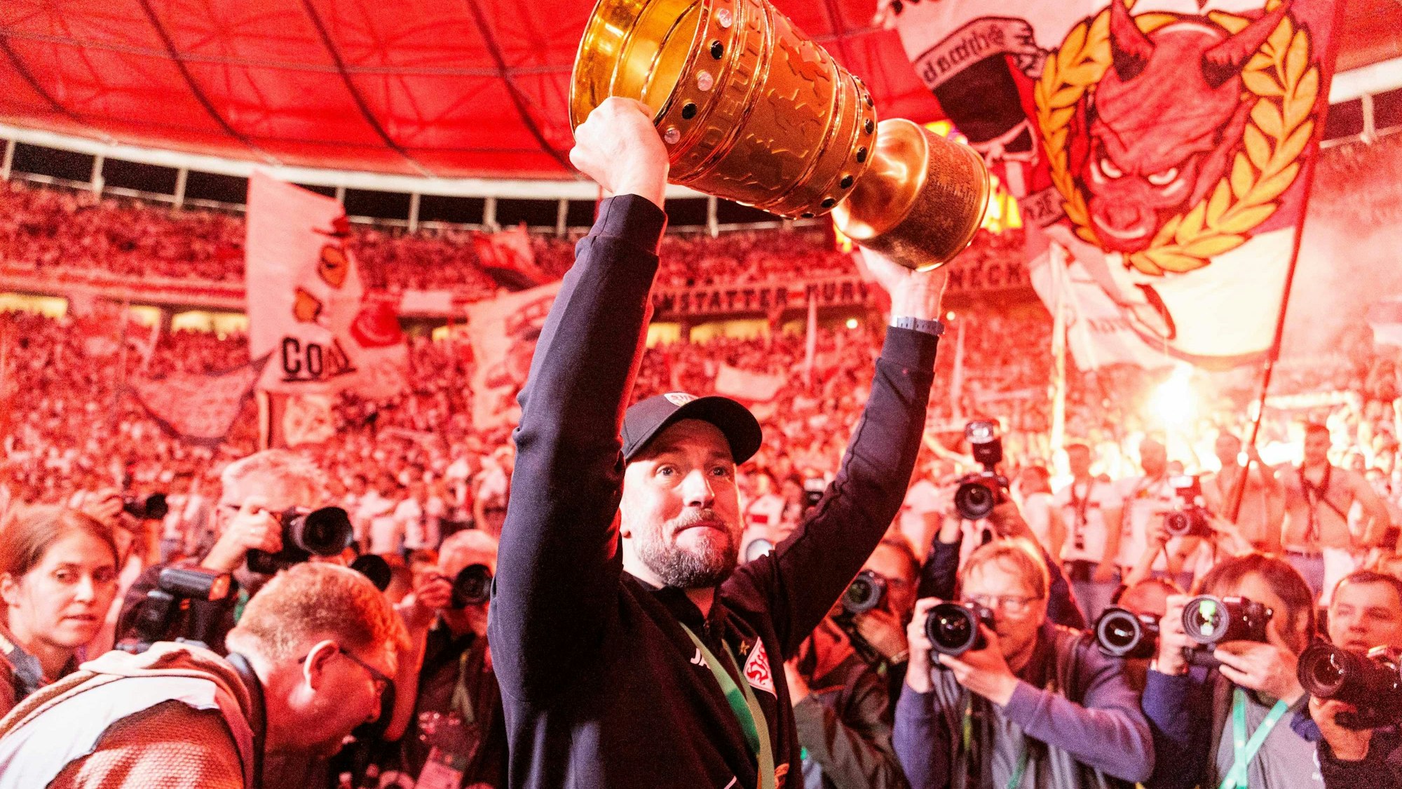 Sebastian Hoeneß, Cheftrainer VfB Stuttgart, hält vor der Kurve den Pokal hoch