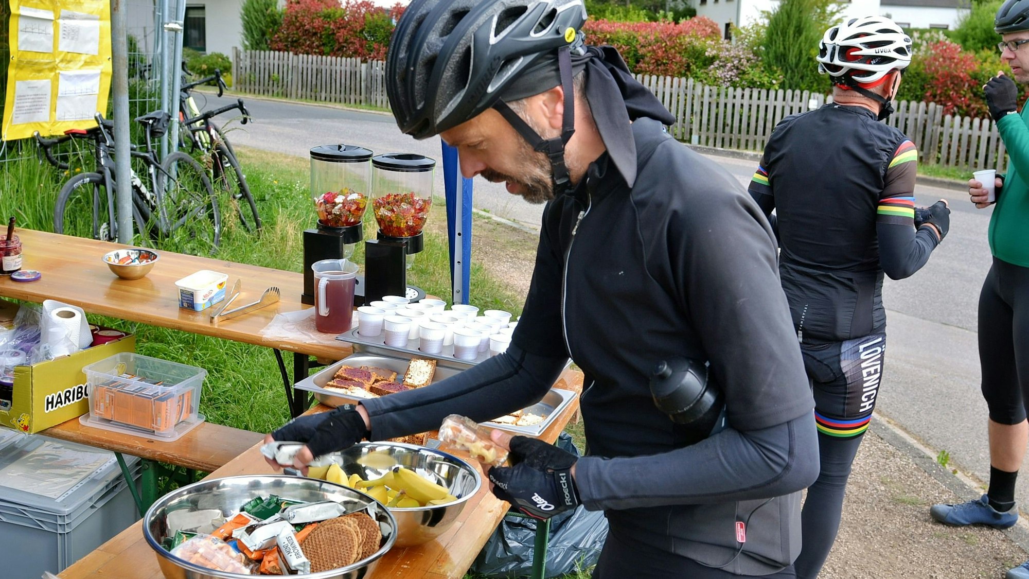 Teilnehmer Marco vom Hau, der in voller Radfahrermontur samt Helm ist, holt sich an einem Streckenposten ein paar Snacks zur Stärkung.