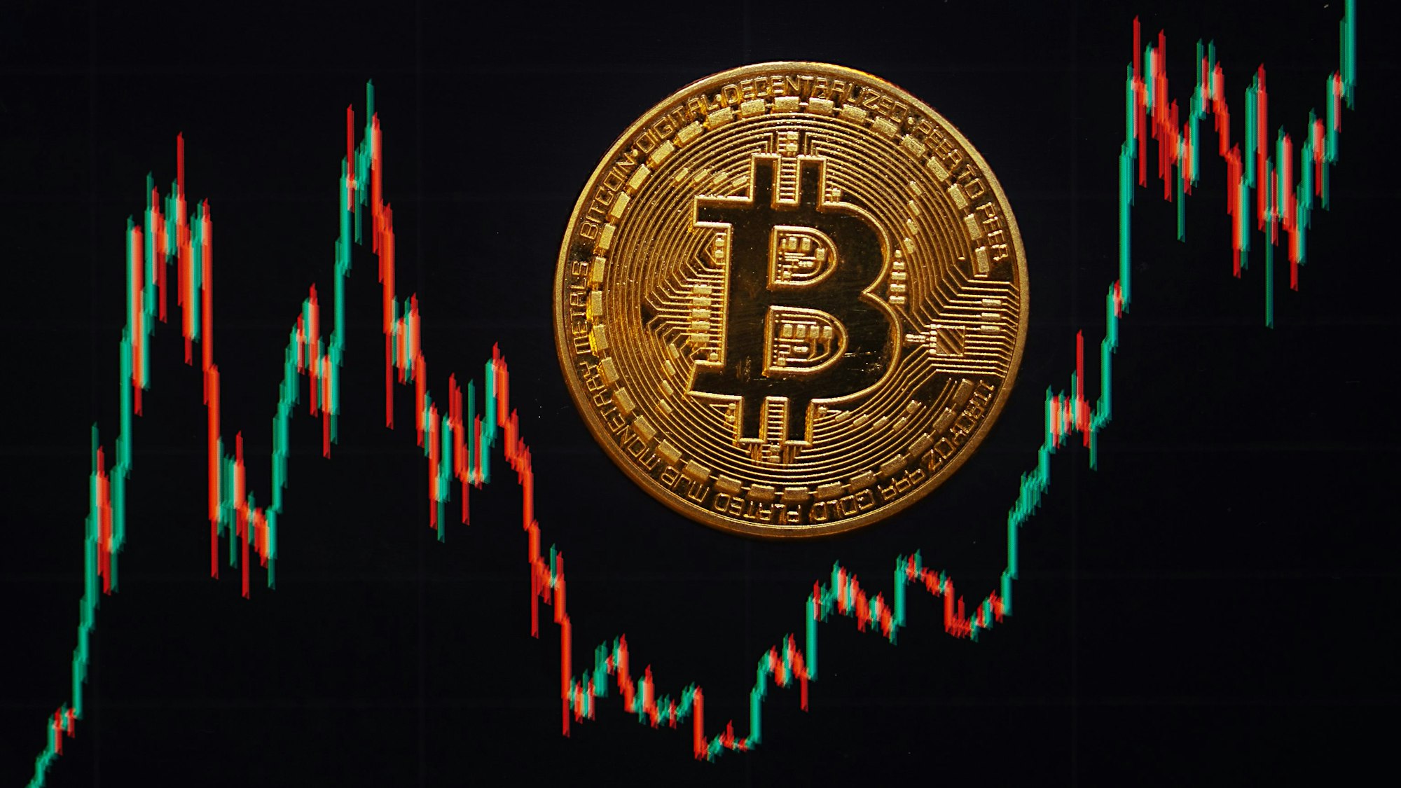 Eine Bitcoin-Münze liegt auf einem Bildschirm, der den Bitcoin - US-Dollar Kurs zeigt.